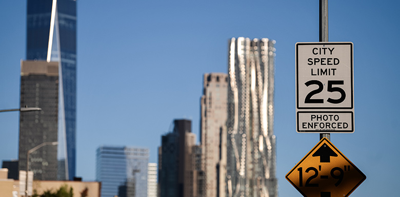 25 miles per hour speed limit sign with view of New York city skyline behind the sign